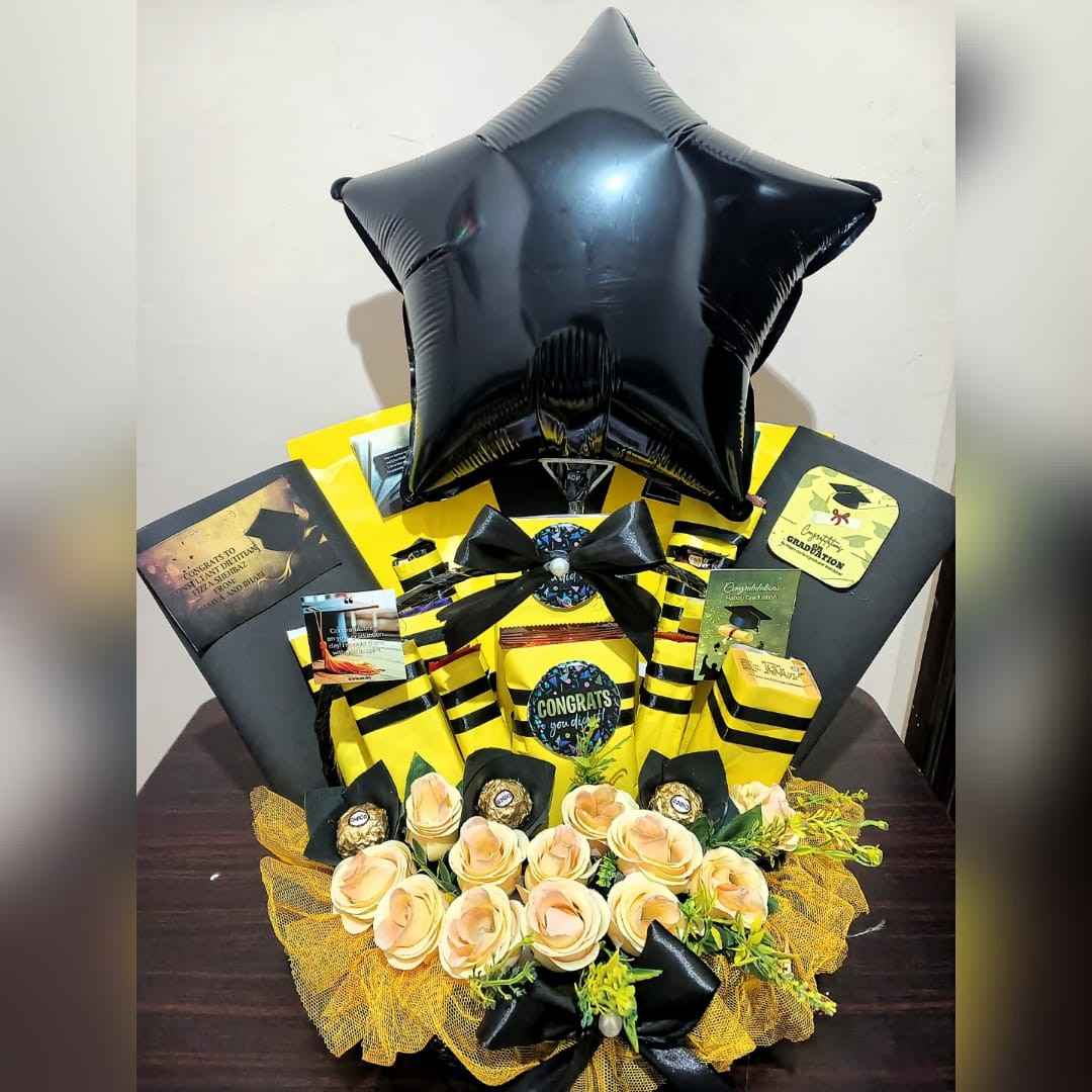 Graduation-themed gift arrangement with a black star balloon, yellow and black accents, Ferrero Rocher chocolates, roses, and congratulatory messages for the graduate.