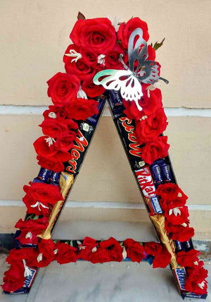 Creative letter "A" decoration with red roses, KitKat, Mars, and Dairy Milk chocolates, accented by a silver butterfly for a personalised and elegant gift.