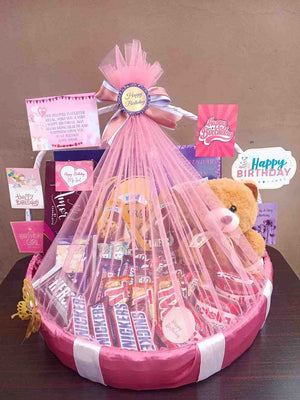 Pink-themed birthday gift basket featuring Snickers, Twix chocolates, a teddy bear, personalised birthday messages, and decorative ribbons for a festive touch.