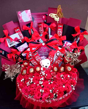 Elegant birthday gift basket featuring red roses, KitKat and Ferrero Rocher chocolates, a cute teddy bear, red bows, and a golden butterfly decoration.