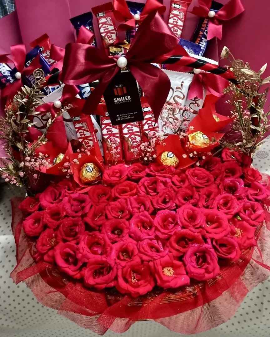 Luxurious red rose arrangement with chocolates, including KitKat and Ferrero Rocher, adorned with elegant red bows and festive embellishments. Perfect gift.