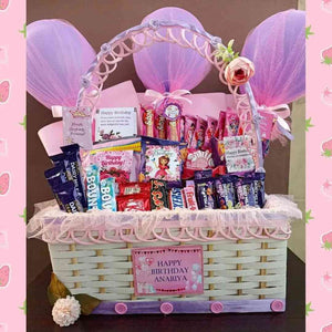 Adorable birthday gift basket with Dairy Milk, Bounty, KitKat chocolates, pink decorations, balloons, and a personalised message for a delightful celebration.