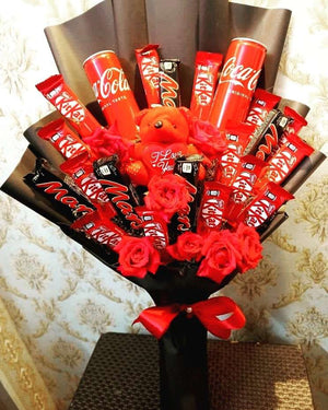 Unique bouquet featuring Coca-Cola cans, KitKat, Mars chocolates, red roses, and a teddy bear, wrapped in black paper with a red bow for a stylish gift.