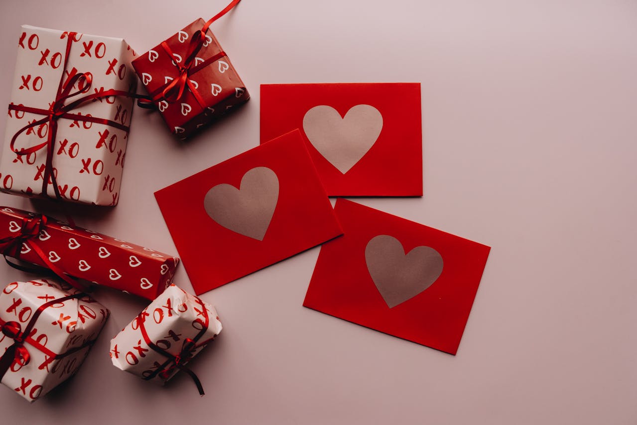 Romantic gift setup with heart-themed red envelopes and beautifully wrapped presents adorned with red ribbons. Perfect for Valentine’s Day or special occasions.